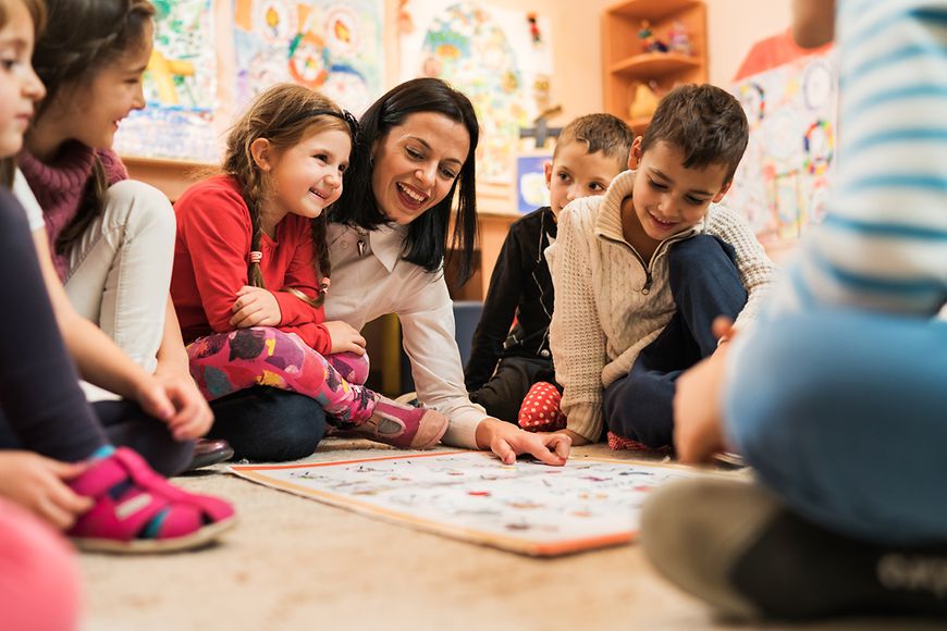 Eine Frau und mehrere kleine Kinder in einer spielerischen Lernsituation