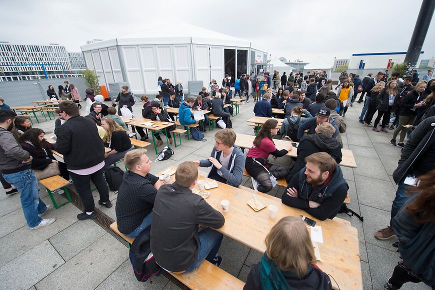 Junge Erwachsene sitzen auf Bierbänken vor dem Jugenparlament