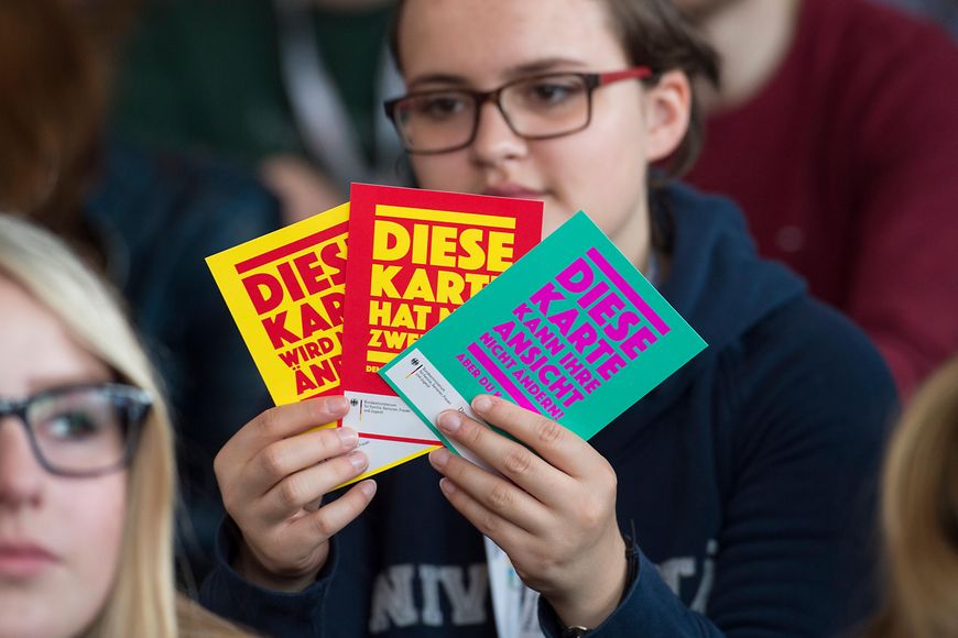 Junges Mädchen hält drei Flyer der Kampagne "Demokratie leben!" in der Hand