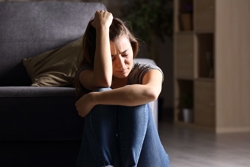 Junge Frau sitzt mit traurigem Gesicht auf dem Boden, stützt ihren Kopf auf