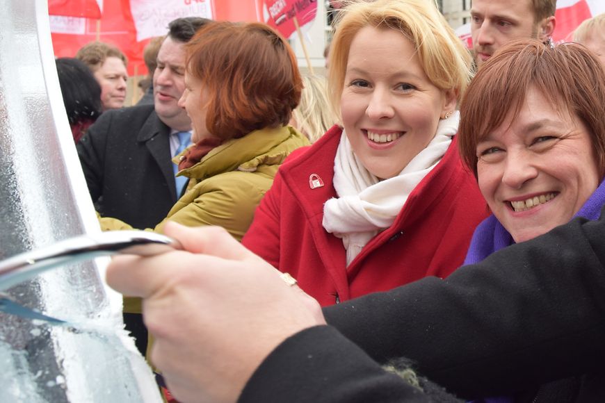 Dr. Franzsika Giffey und Caren Marks schauen in die Kamera. Im Vordergrund wird ein Eisblock angesägt 