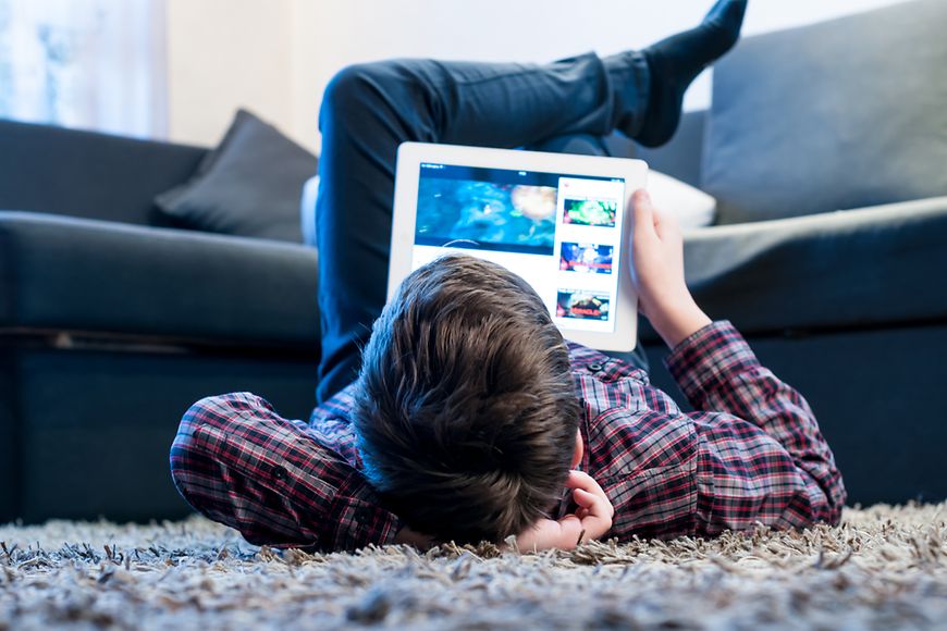 Junge liegt mit Tablet auf dem Boden 