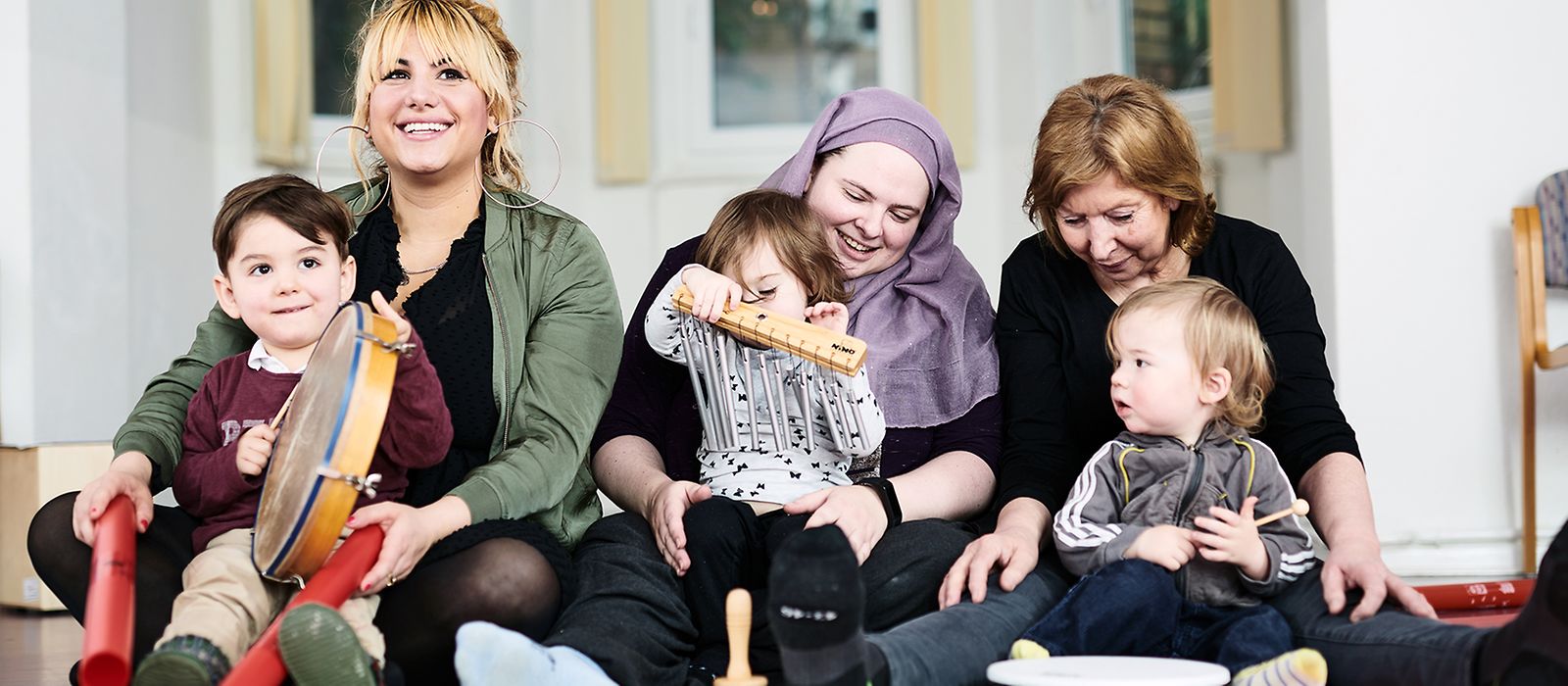 Drei Frauen verschiedenen Alters sitzen mit drei Kindern auf dem Boden