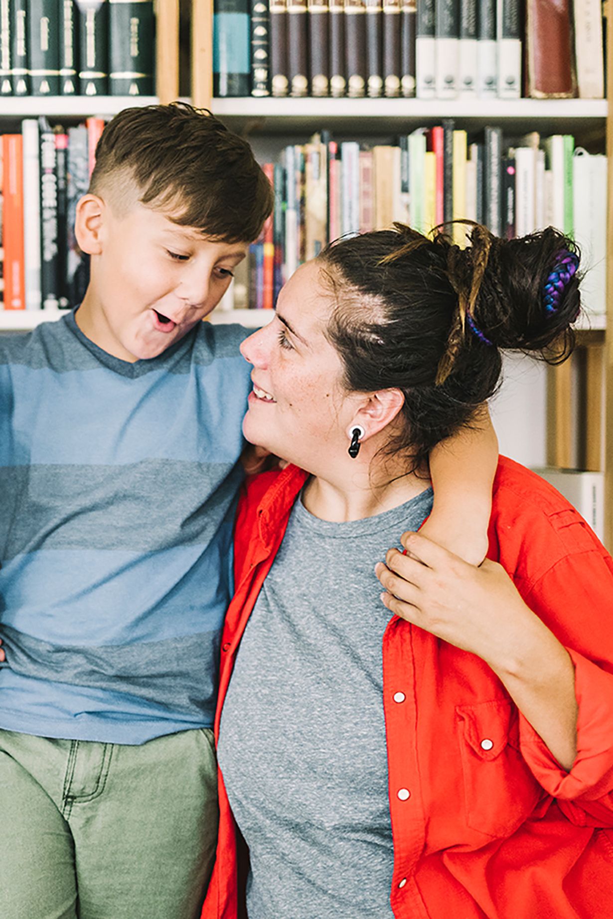 Ein Junge legt den Arm um seine Mutter, die ihn vor einer Bücherwand hochhebt