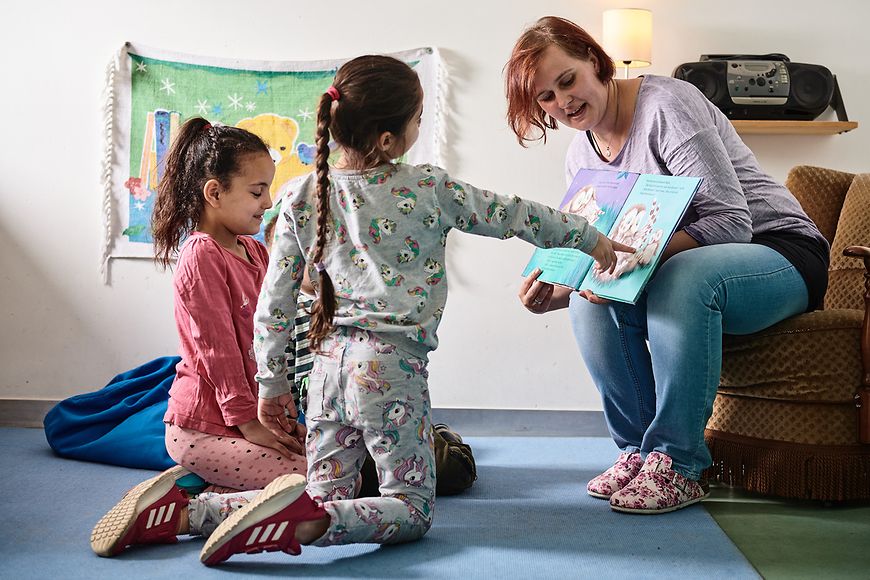 Eine Erzieherin schaut sich in der Kita mit Kindern ein Buch an.