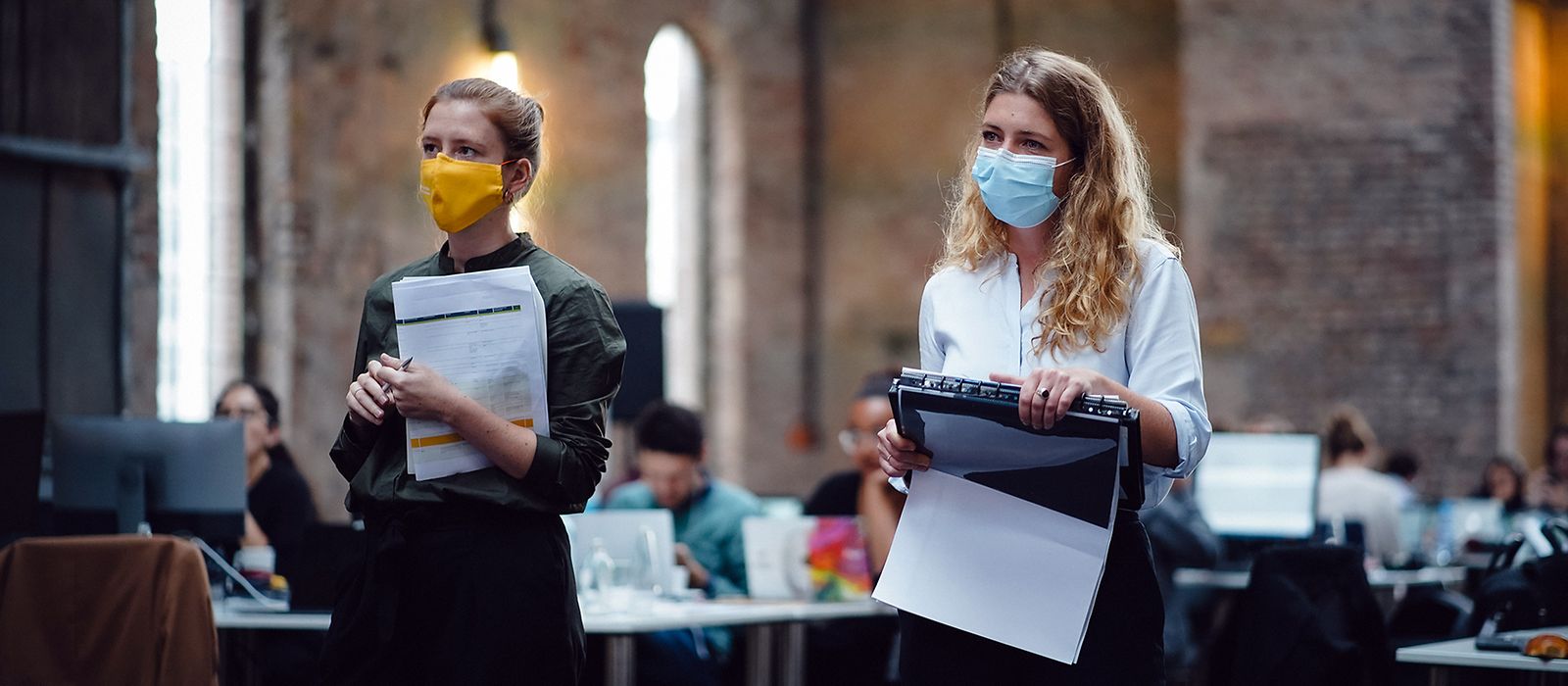 Zwei Frauen mit Maske tragen Unterlagen