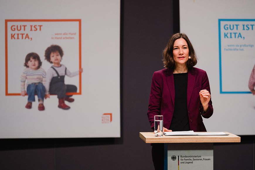 Anne Spiegel bei der Fachkonferenz mit einer Kachel im Hintergrund: Gut ist Kita, wenn alle Hand in Hand arbeiten