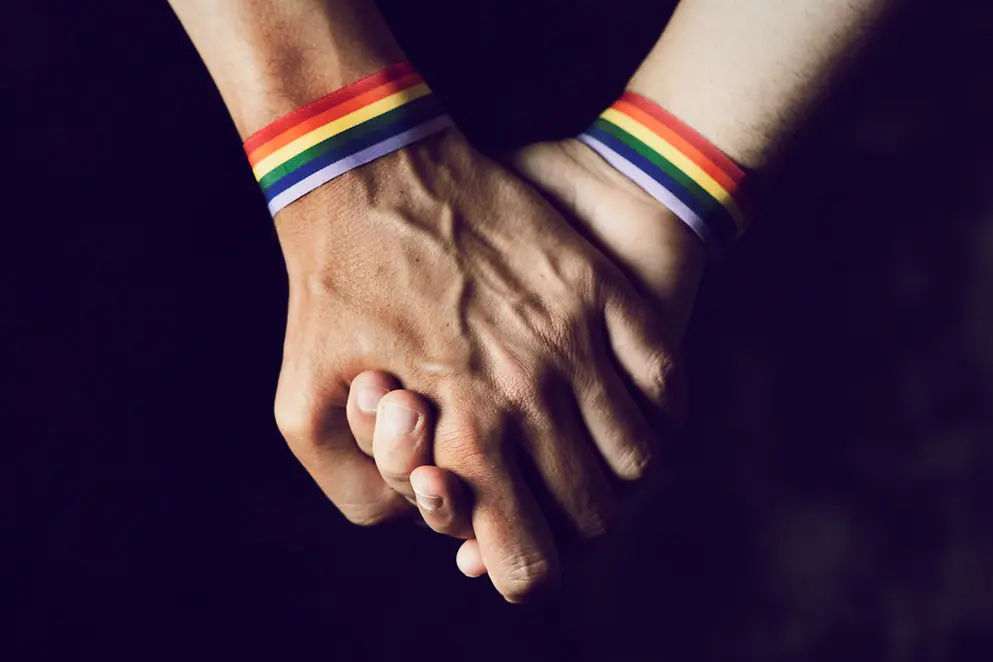 Zwei Menschen mit Armband in Regenbogenfarben nehmen sich an die Hand 