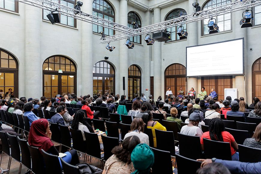 Teilnehmende der Veranstaltung. Diagonale Ansicht auf Bühne mit Leinwand