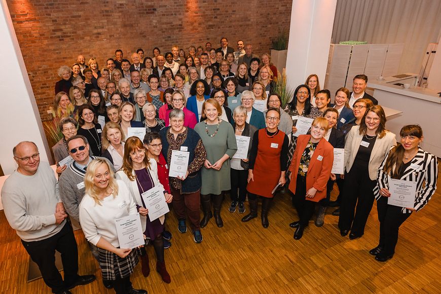 Ein Gruppenfoto mit Lisa Paus und weiteren Personen. Einige von ihnen halten Urkunden in der Hand.