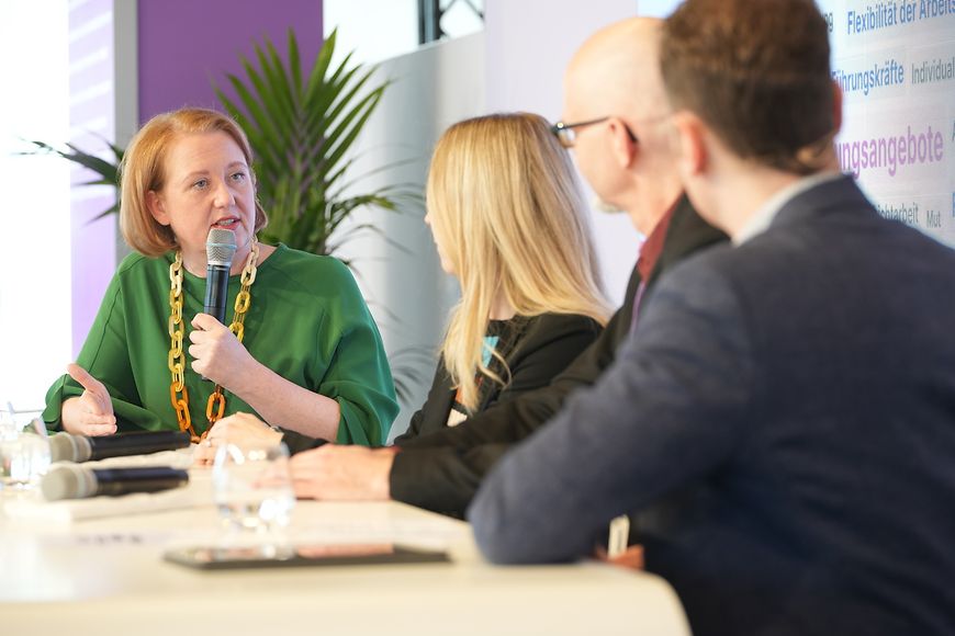 Lisa Paus diskutiert mit anderen Teilnehmern der Podiumsdiskussion an einem Tisch