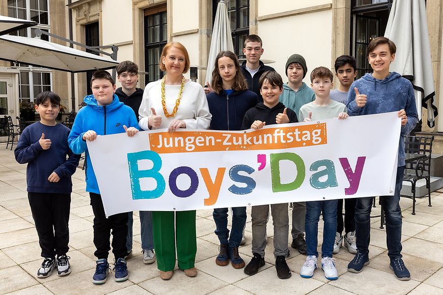 Lisa Paus und eine Gruppe Jugendlicher stehen vor einem Boys-Day-Banner