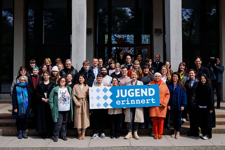 Eine Gruppe steht vor einem Gebäude und hält ein Plakat mit der Aufschrift "Jugend erinnert".