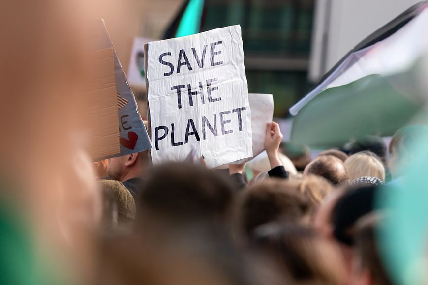 Auf einem Plakat, das aus einer Menschenmenge hochgehalten wird, steht "Save the Planet"