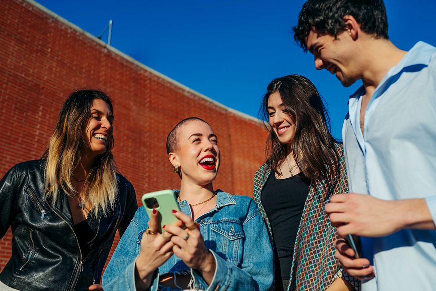 Eine Gruppe von Jugendlichen lacht über etwas, das auf einem Handy zu sehen ist