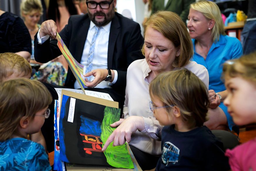 Lisa Paus sitzt mit Kindern auf dem Boden. Im Hintergrund spielt jemand Gitarre