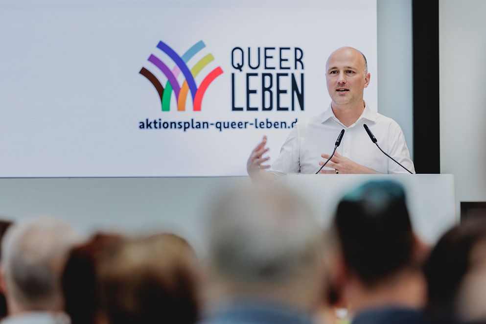 Der Queer-Beauftragte der Bundesregierung Sven Lehmann spricht auf einer Bühne. Im Hintergrund das Logo von "Queer leben"