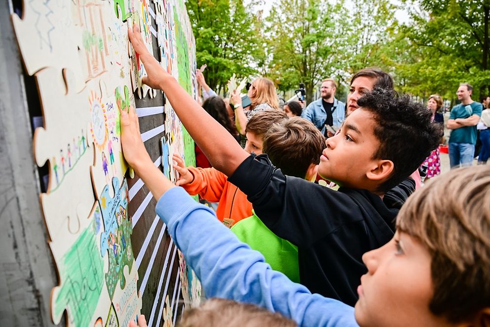 Kinder stehen vor einer Wand mit großen Puzzleteilen 