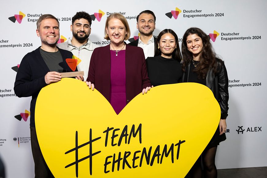 Gruppenfoto von Lisa Paus und den Preisträgerinnen und Preisträgern, sie halten ein gelbes Herz, auf dem "Team Ehrenamt" steht