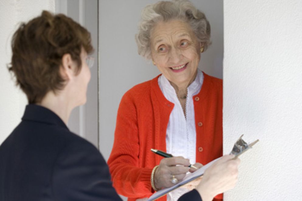 Älterer Dame steht an der Hasutür und unterschreibt einen Vertrag.