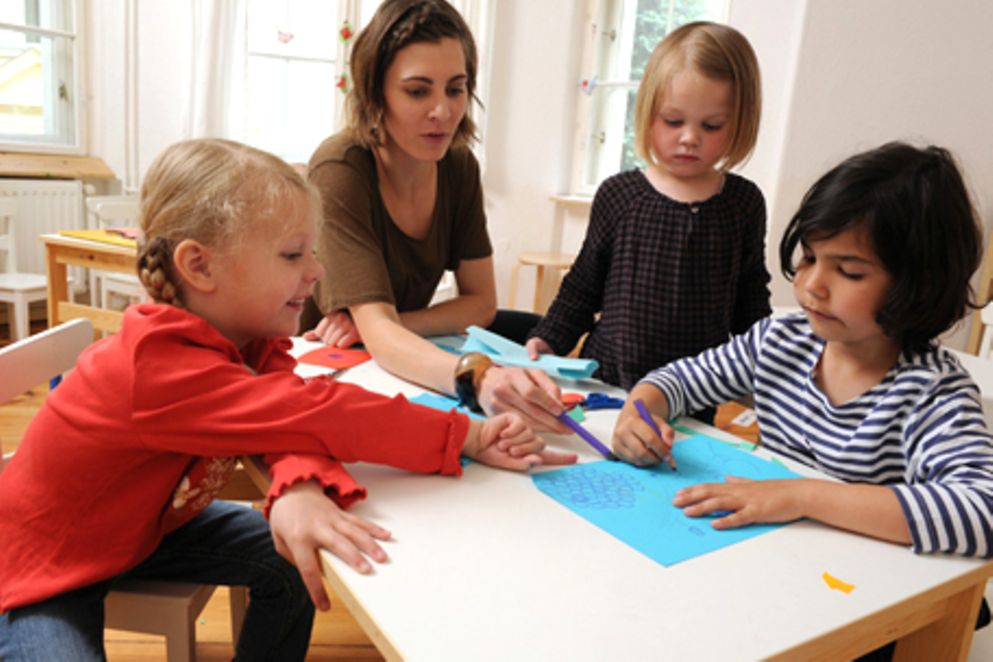 Eine Betreuerin und drei Kinder beim Malen in einer Kita. Bildquelle: M. Gronau / BMFSFJ