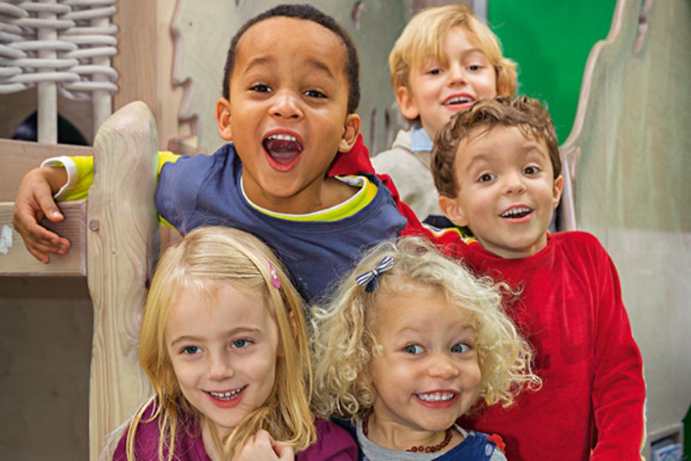 Fünf kleine Kinder spielen lachend in einer Kita.