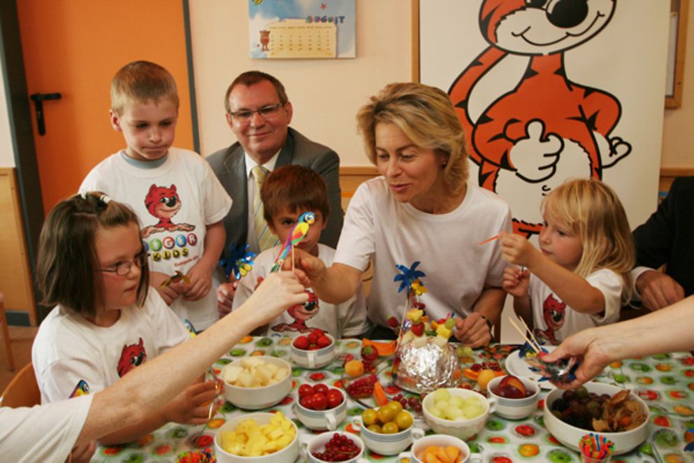 Ursula von der Leyen und der AOK-Bundesvorsitzende Herbert Reichelt essen gemeinsam mit einer Gruppe Kinder.