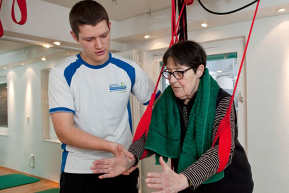 Ein junger Mann leitet eine Patientin beim Rehabilitationssport an, Bildnachweis: BMFSFJ